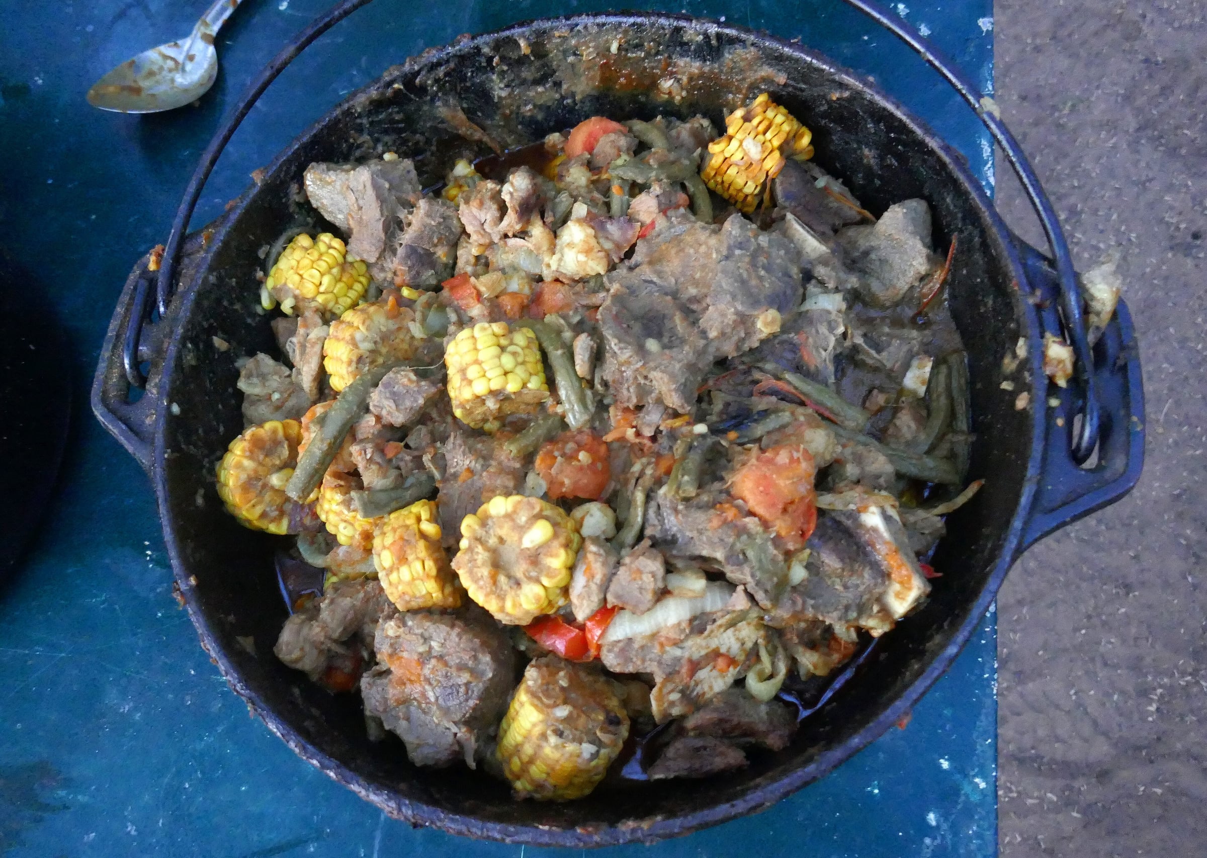 A three-legged cast-iron potjie filled with meat, mielies and vegetables
