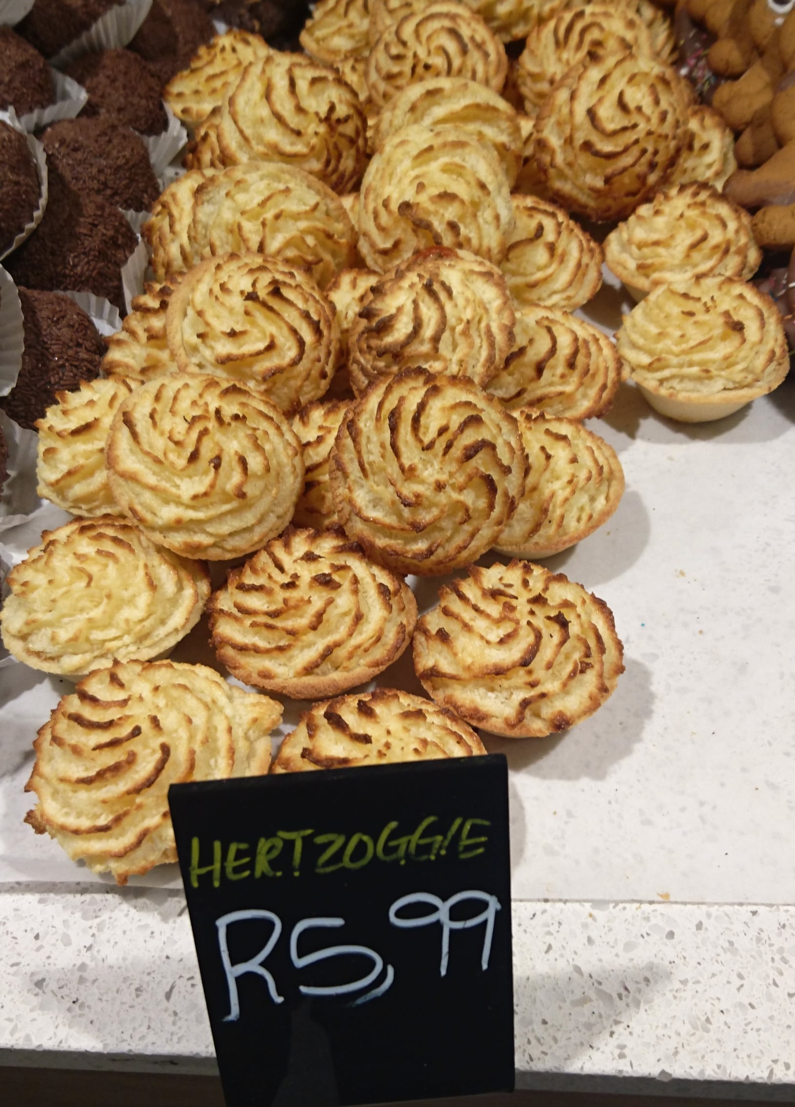 A tray of hertzoggies with piped coconut meringue tops on a bakery counter