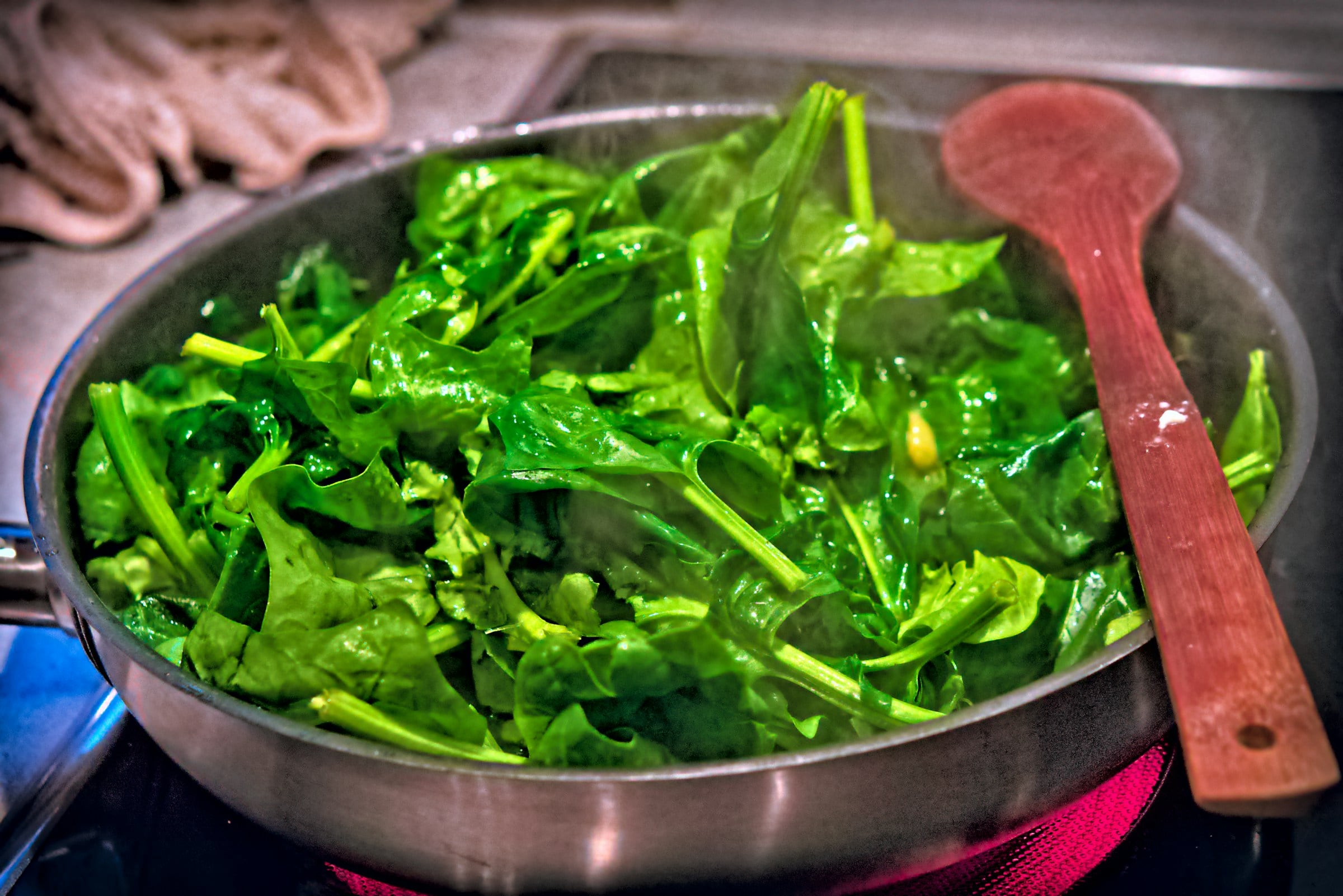 Bright green spinach wilting in a pan with a red wooden spoon