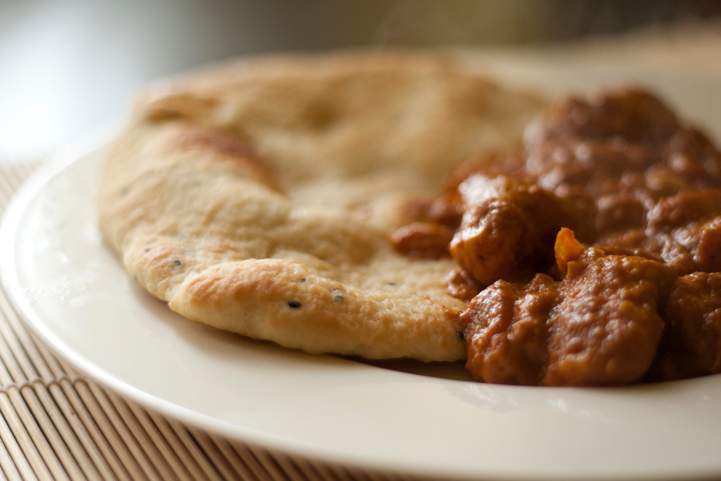 A bowl of butter chicken in an orange sauce served with naan bread