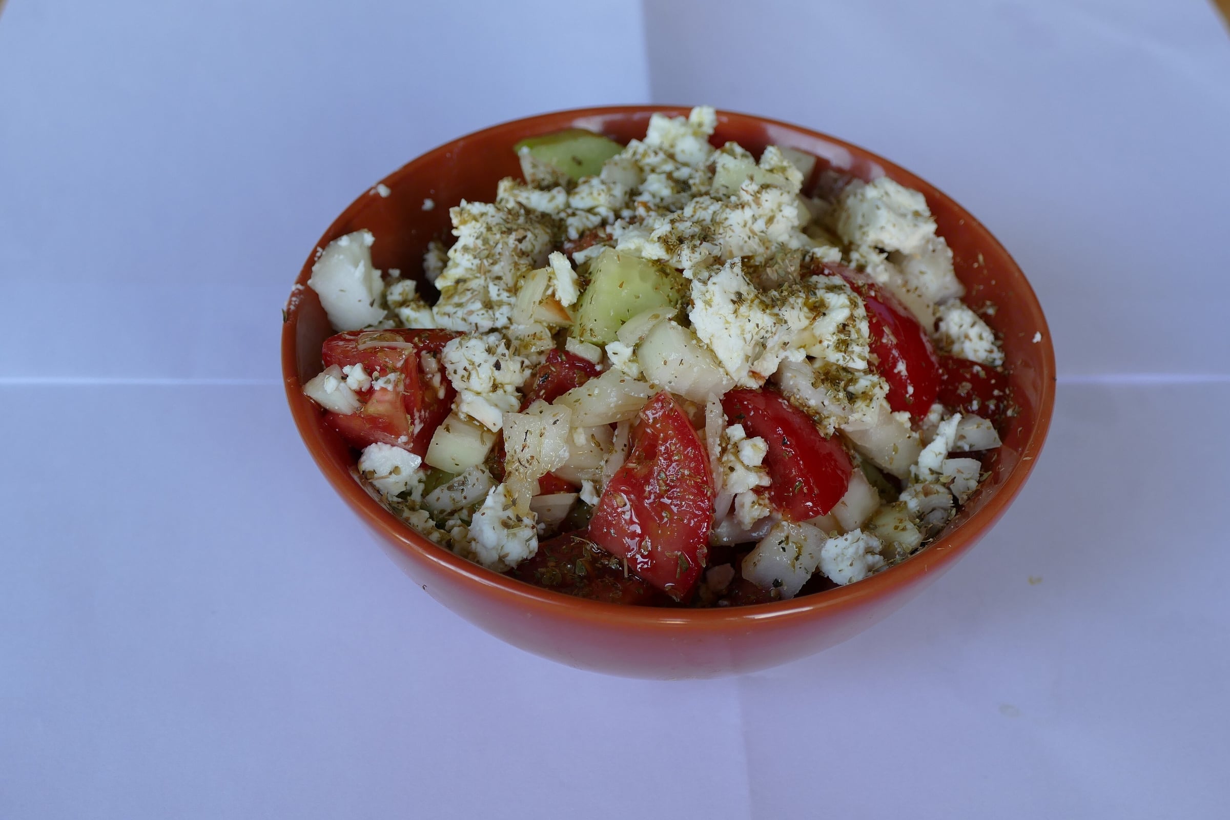 A bowl of Greek salad: tomato, cucumber and onion topped with crumbled feta and dried oregano